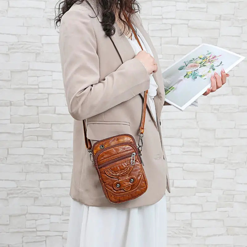 Simples Market brown PU leather crossbody messenger bag with zip pockets, worn by a woman in a beige coat