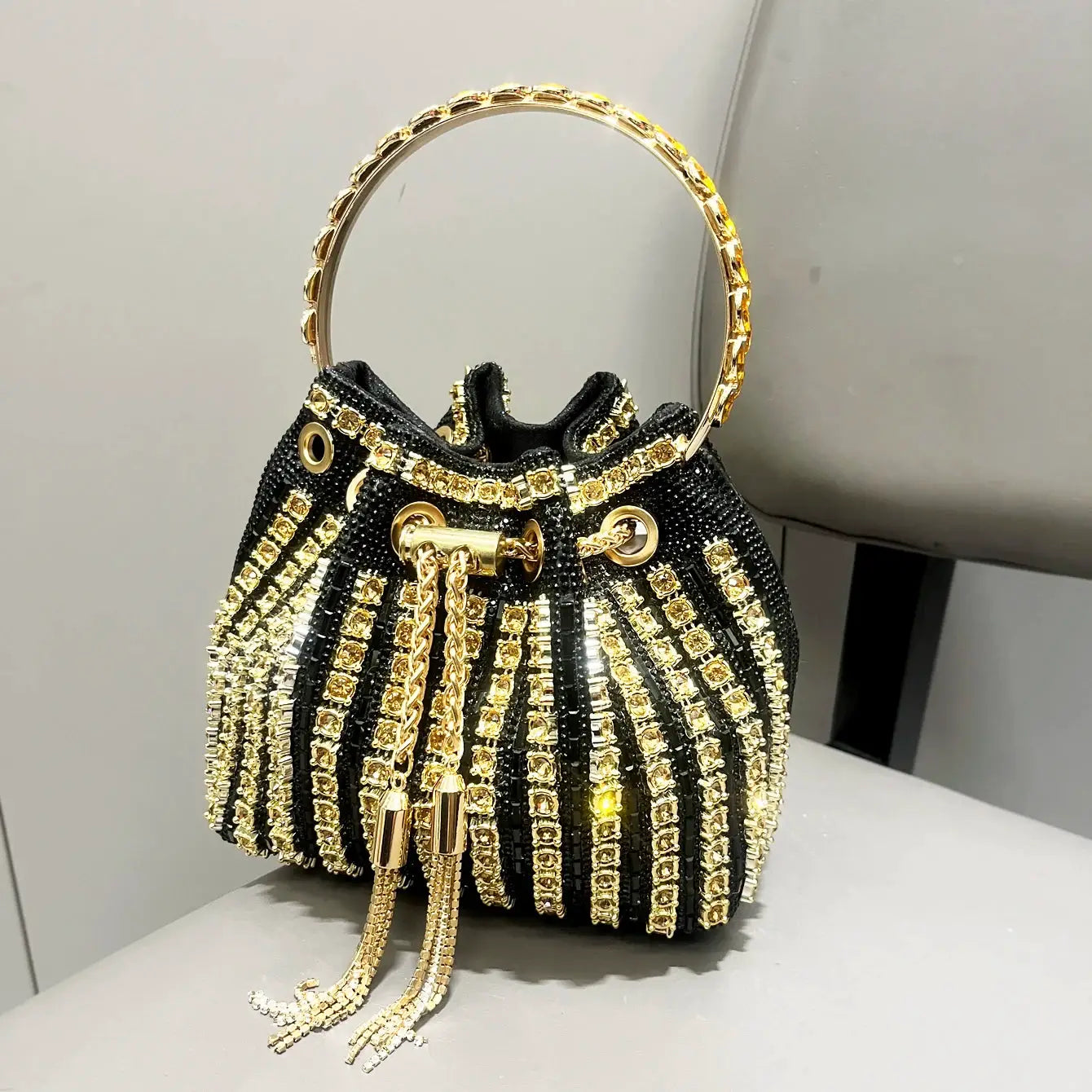 Black beaded bucket clutch with gold rhinestones, circular gold handle, and tassel chains