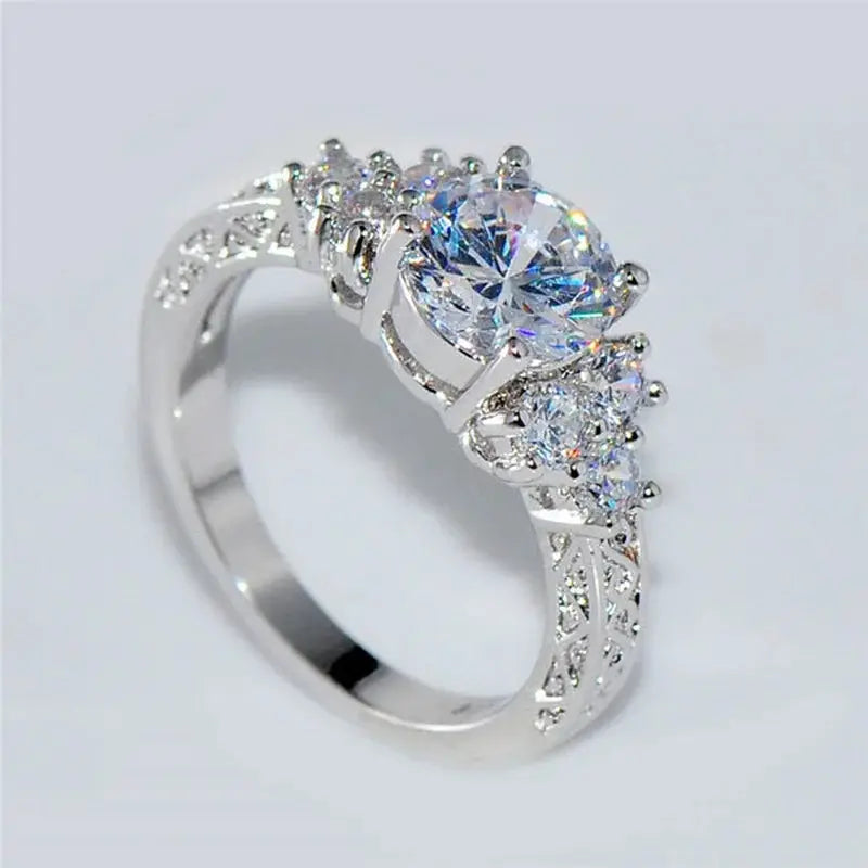 Silver engagement ring with a large central white zircon and two side stones, featuring an intricate filigree band