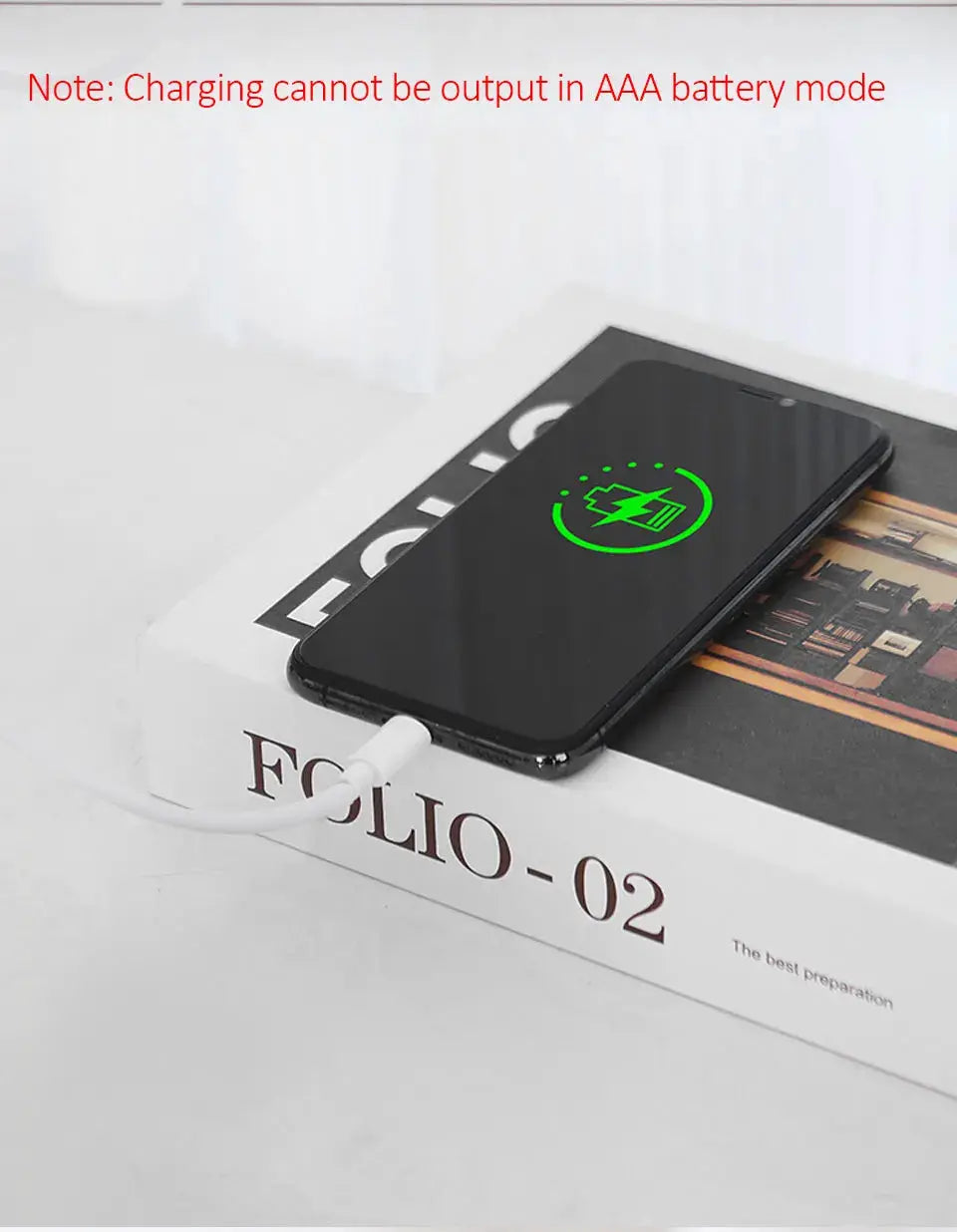 Smartphone on a white desk, black glossy finish, charging via cable with a green charging icon on screen