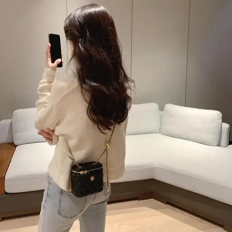 Mini black quilted shoulder bag with gold chain crossbody worn by woman in cream sweater