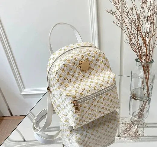 Women's white backpack with gold polka-dot pattern, front zip pocket, top handle, adjustable straps