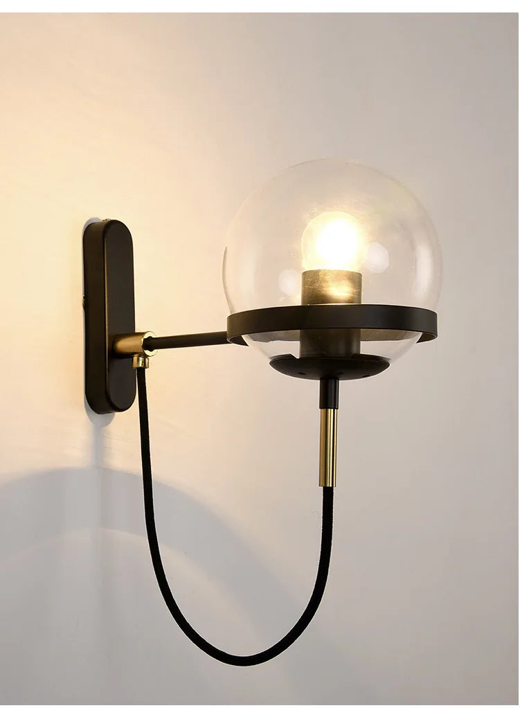Modern glass ball wall lamp in black metal with clear globe and brass accents, E27 bulb.