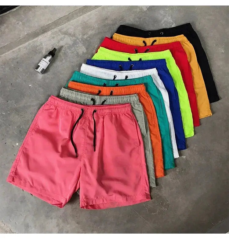 Simples Market men's swim shorts set in assorted colors; pink front pair with gray and other colorful trunks behind.