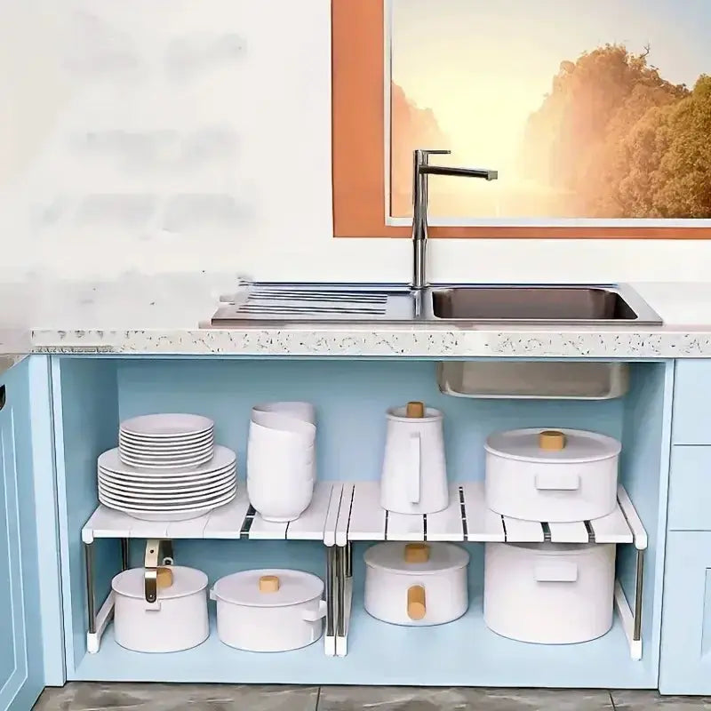 Stackable storage rack wardrobe organizer with white slatted shelves under a kitchen sink in a light blue cabinet