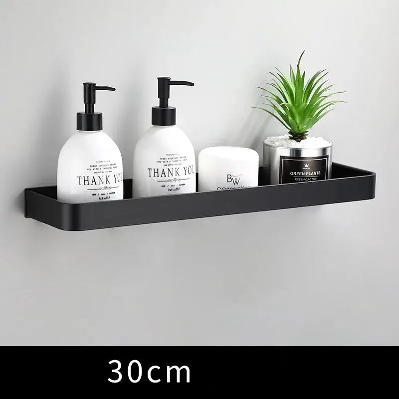 Bathroom shelf wall-mounted in black aluminum, 30 cm, holding two pump bottles, a jar and a small plant.