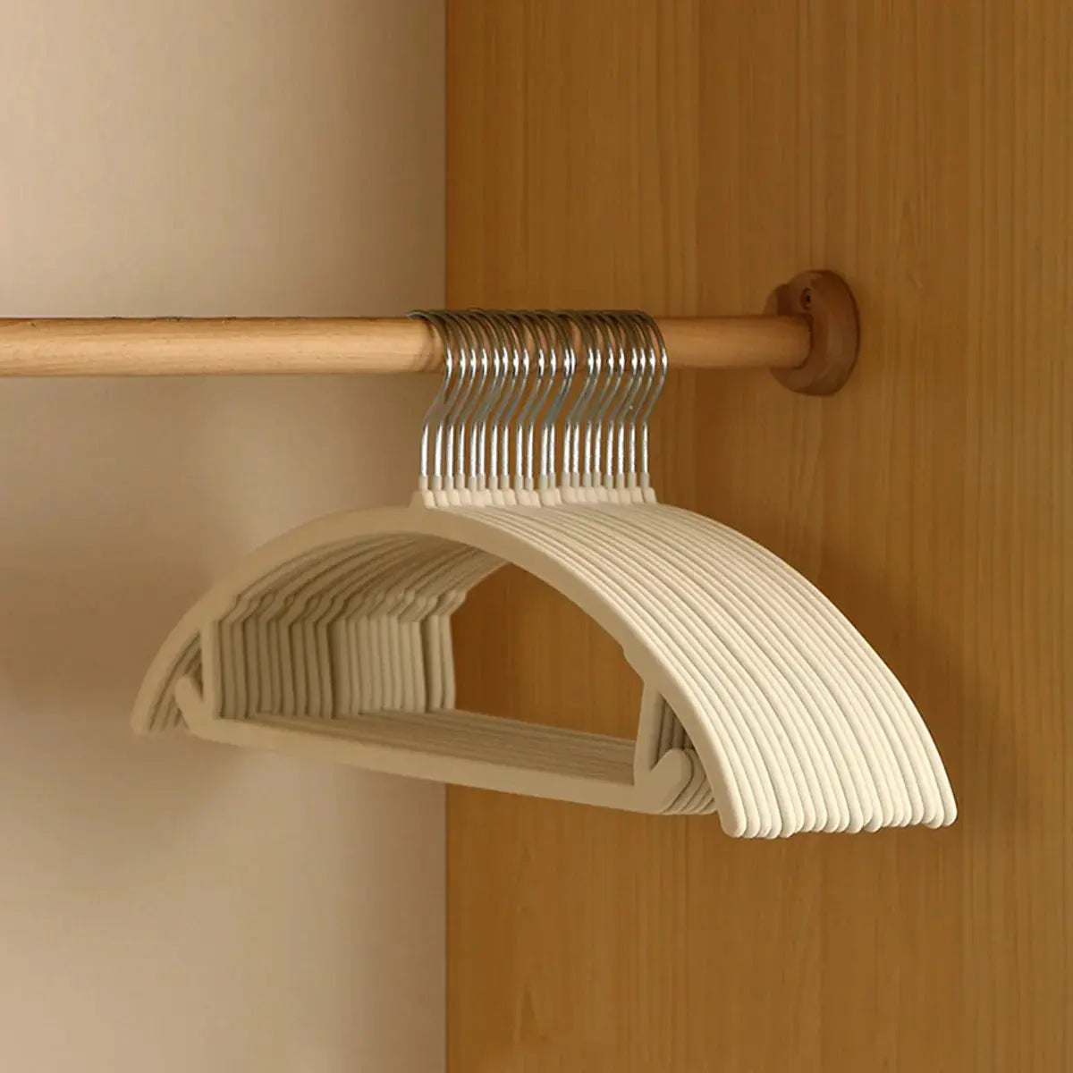 Set of white plastic hangers with metal hooks on a wooden closet rod