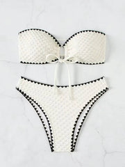 Two-piece white strapless bandeau bikini with textured fabric, black zigzag trim and bow detail.