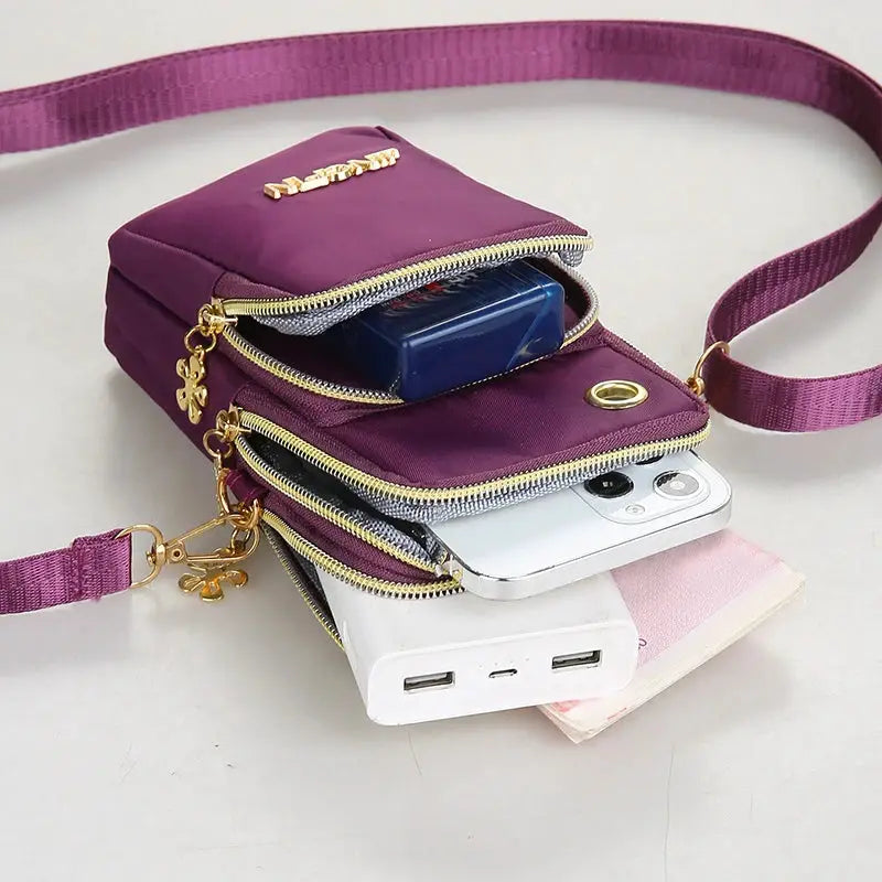 Mobile phone bag by Simples Market, purple crossbody mini bag with gold zippers and pockets; shown with smartphone.