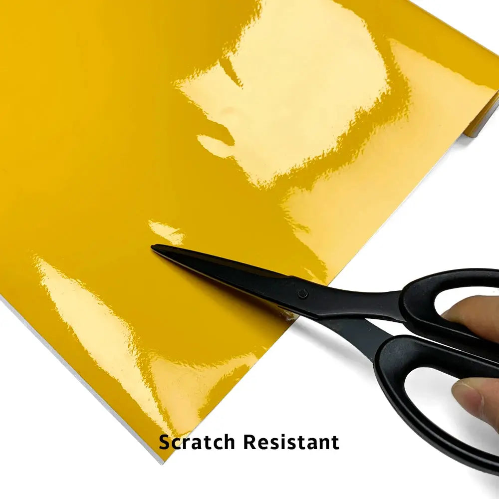 Glossy yellow car vinyl wrap sheet, scratch-resistant; scissors cutting it.
