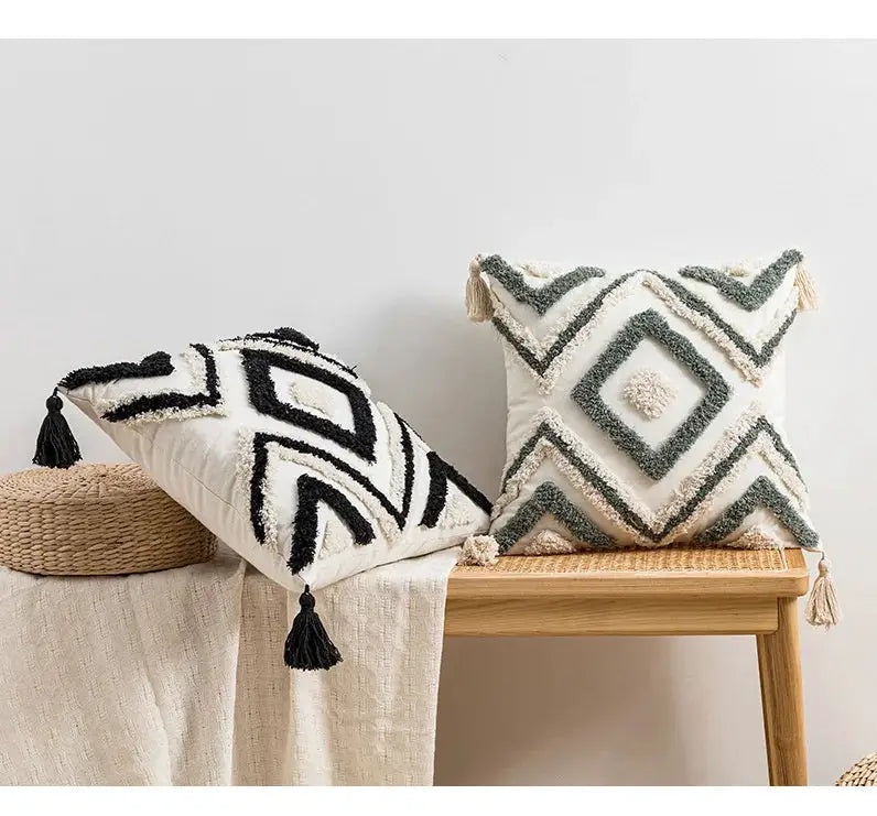 Two boho tufted decorative pillows with white bases and black and teal diamond patterns, tassels, on a wooden bench