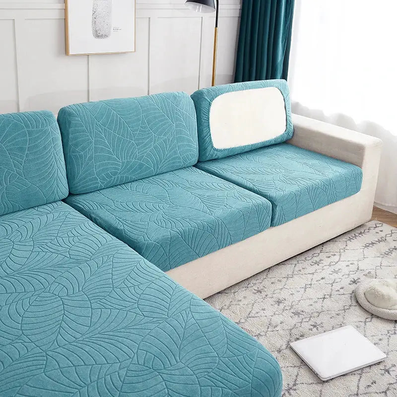Three teal waterproof stretch seat cushion covers with leaf pattern on beige sofa