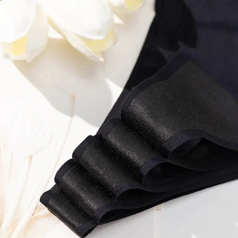 Black women's thong underwear with layered satin ruffle waistband; close-up fabric detail.