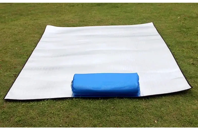 Camping mat by Simples Market with aluminum foil insulation; reflective silver sleeping pad and blue carry bag on grass