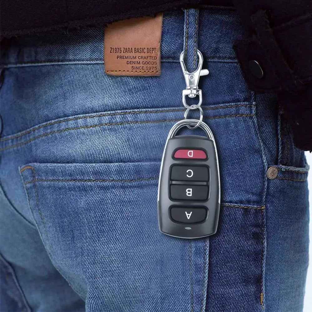 Remote key fob, black plastic body with four buttons including a red top button, attached to a metal keychain
