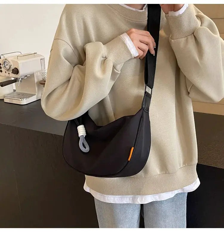 Dumpling-style crossbody bag by Simples Market in black with orange accent and wide strap