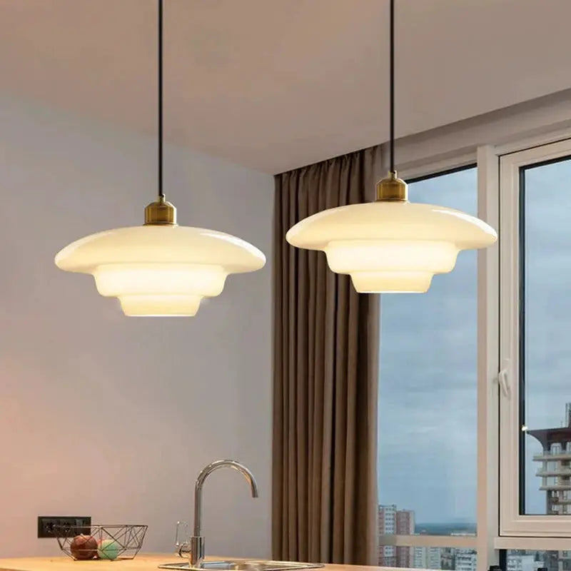 Nordic glass pendant lamps, white layered frosted glass with brass caps, pair hanging over kitchen island.