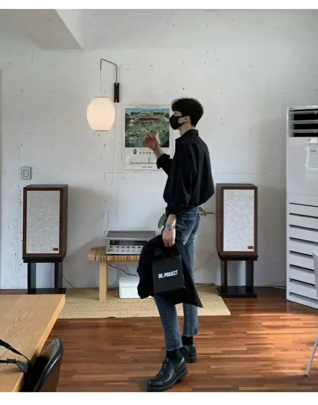 Men's slim-fit black cardigan with long sleeves, modeled in a modern indoor setting with blue jeans