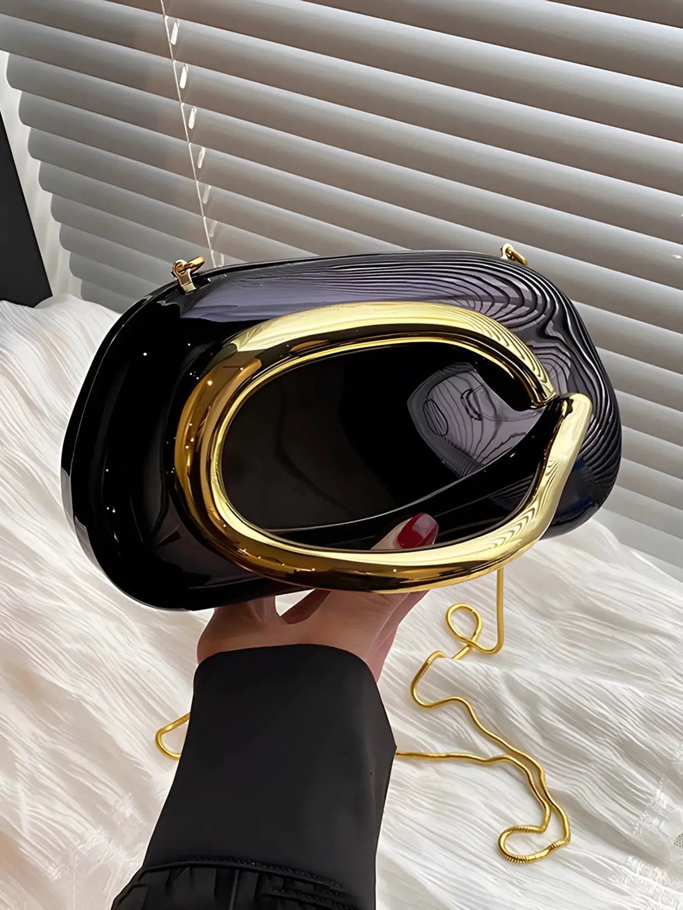 Black acrylic box crossbody bag with a gold-tone curved frame and detachable chain strap