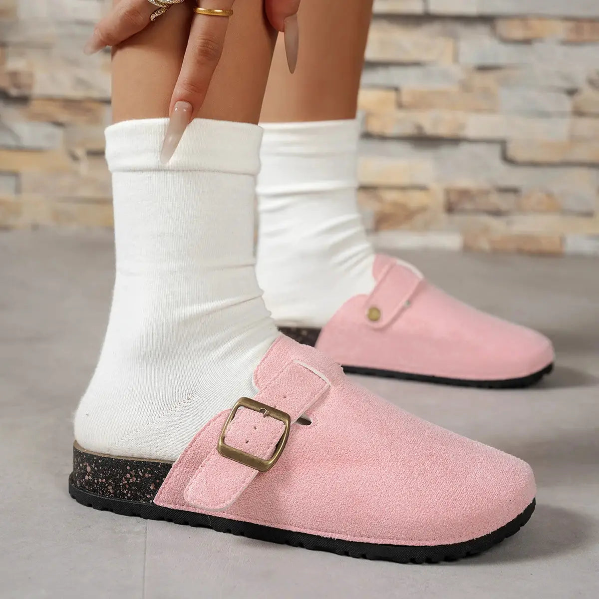 Pink suede buckle slip-on shoes; two in view with white socks and black speckled sole