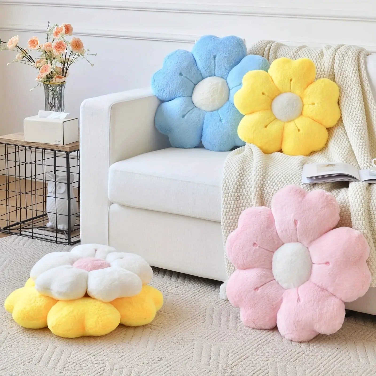 Flower-shaped plush throw pillows in pastel blue, yellow and pink on sofa and floor.