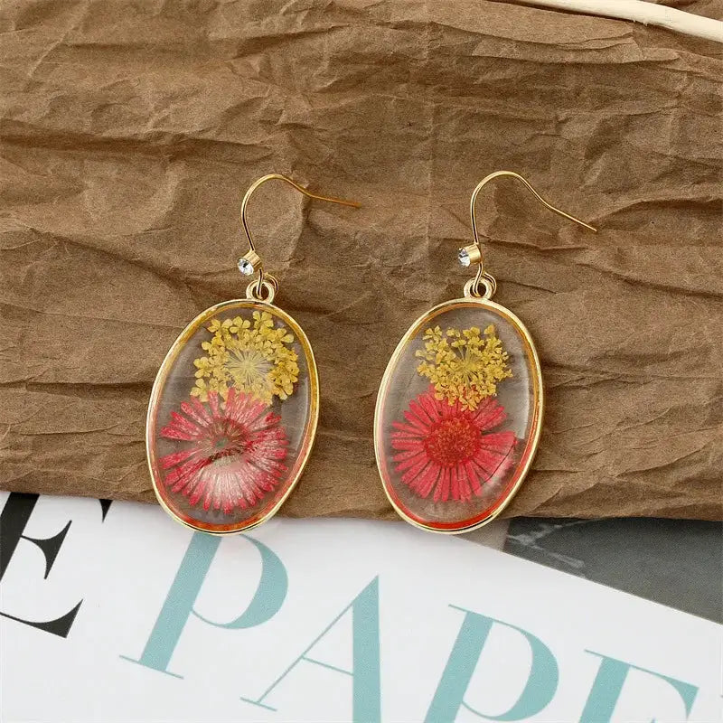 Pair of dangle earrings with gold-tone oval frames, clear epoxy resin encasing colorful pressed flowers