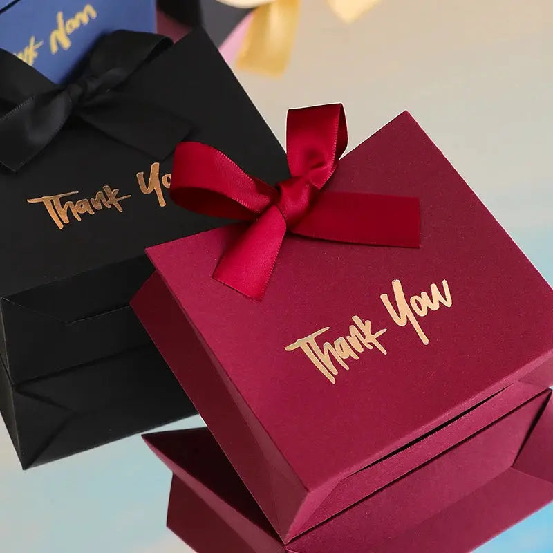 10 mini gift boxes with gold ribbon and Thank You text in magenta, shown with a black gift bag