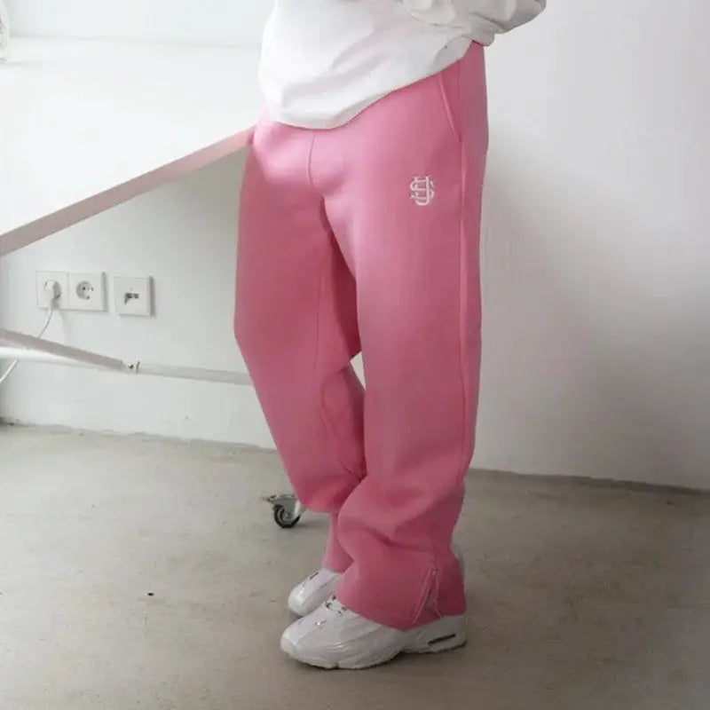 Pink sweatpants with a small white logo on the left thigh, paired with white sneakers.