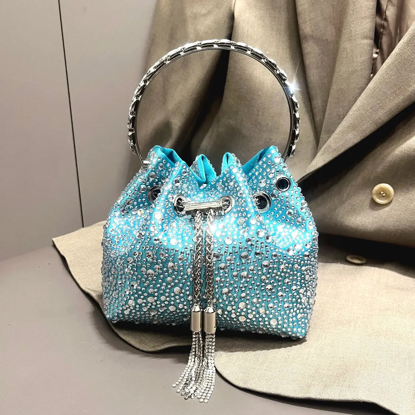 Simples Market blue rhinestone bucket clutch with crystal-studded body, circular silver handle, and tassel cords
