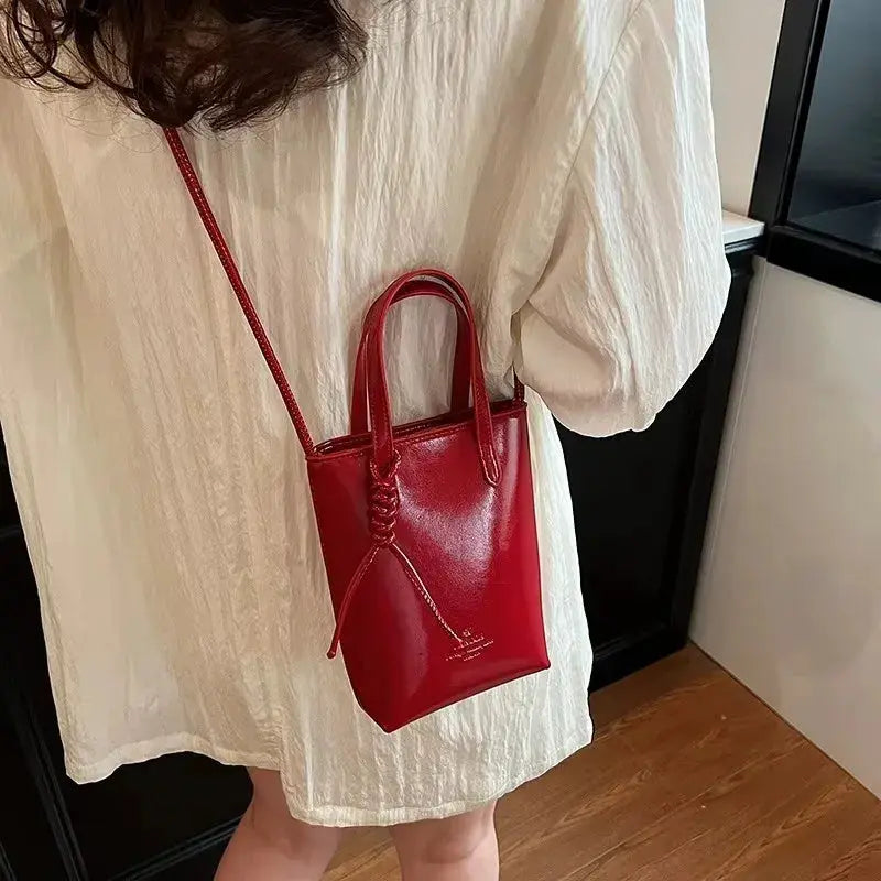 PU leather red mini crossbody bag with top handles and long strap, worn by a woman in a white dress.