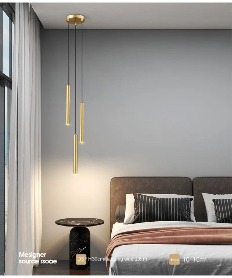 Minimalist bedside pendant lamps; gold cylindrical LED fixtures hanging over a bed in a modern bedroom.