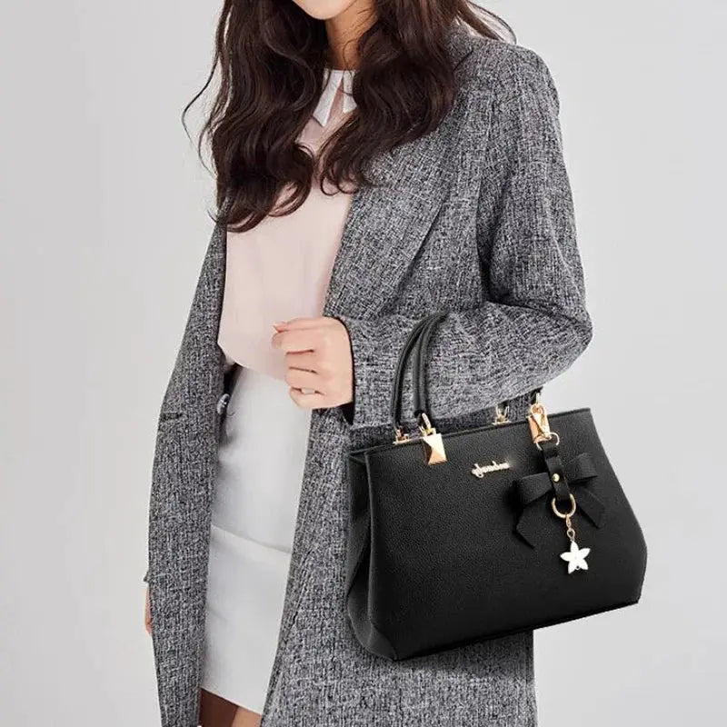 Black handbag with bowknot charm and star pendant, gold hardware, top handles