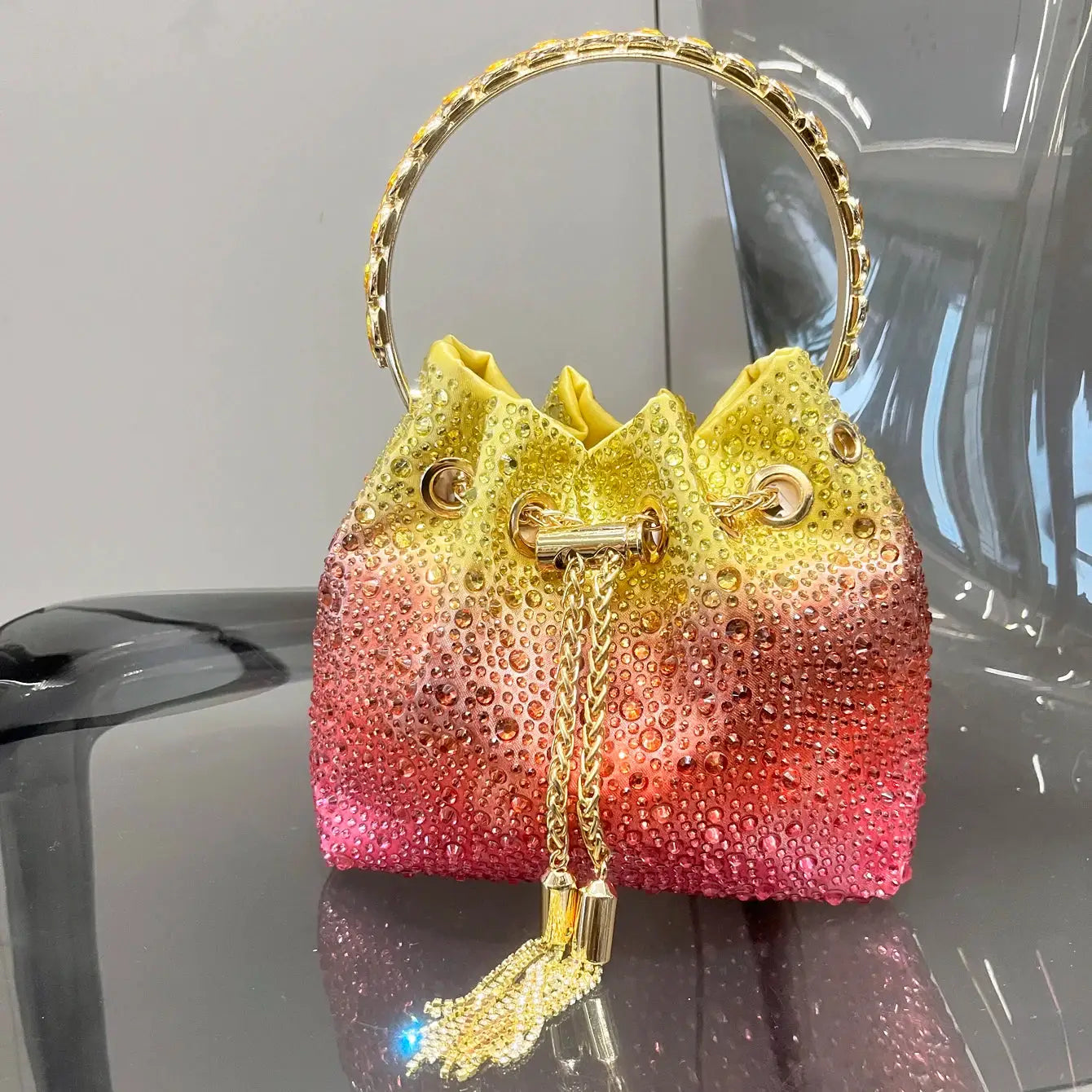 Rhinestone evening clutch with gold ring handle in a yellow-to-pink gradient, crystal-encrusted bucket bag