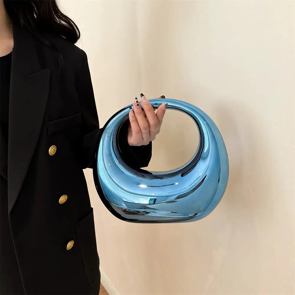Blue metallic PVC round-handle wrist bag clutch, a stylish evening accessory, held by a person in a black blazer.