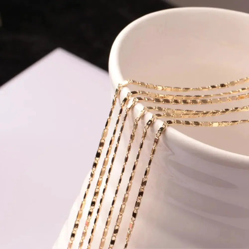 Gold-tone flat 2mm chain necklace, adjustable 40–75cm, five strands draped over a white cup