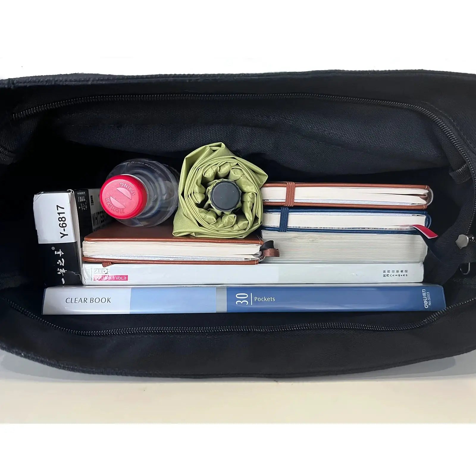 Women's black canvas messenger bag by Simples Market, shoulder bag filled with notebooks and a water bottle.
