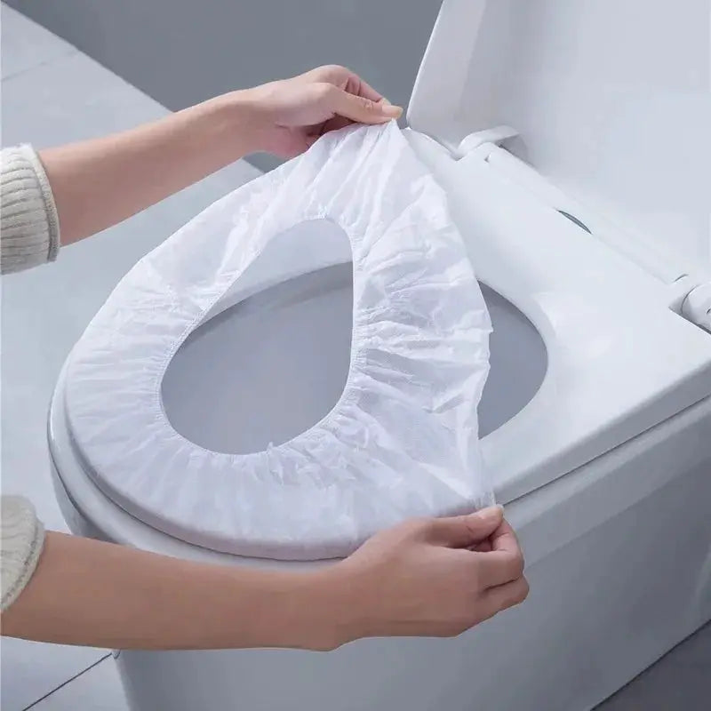 Disposable white non-woven toilet seat cover being placed on a toilet seat.