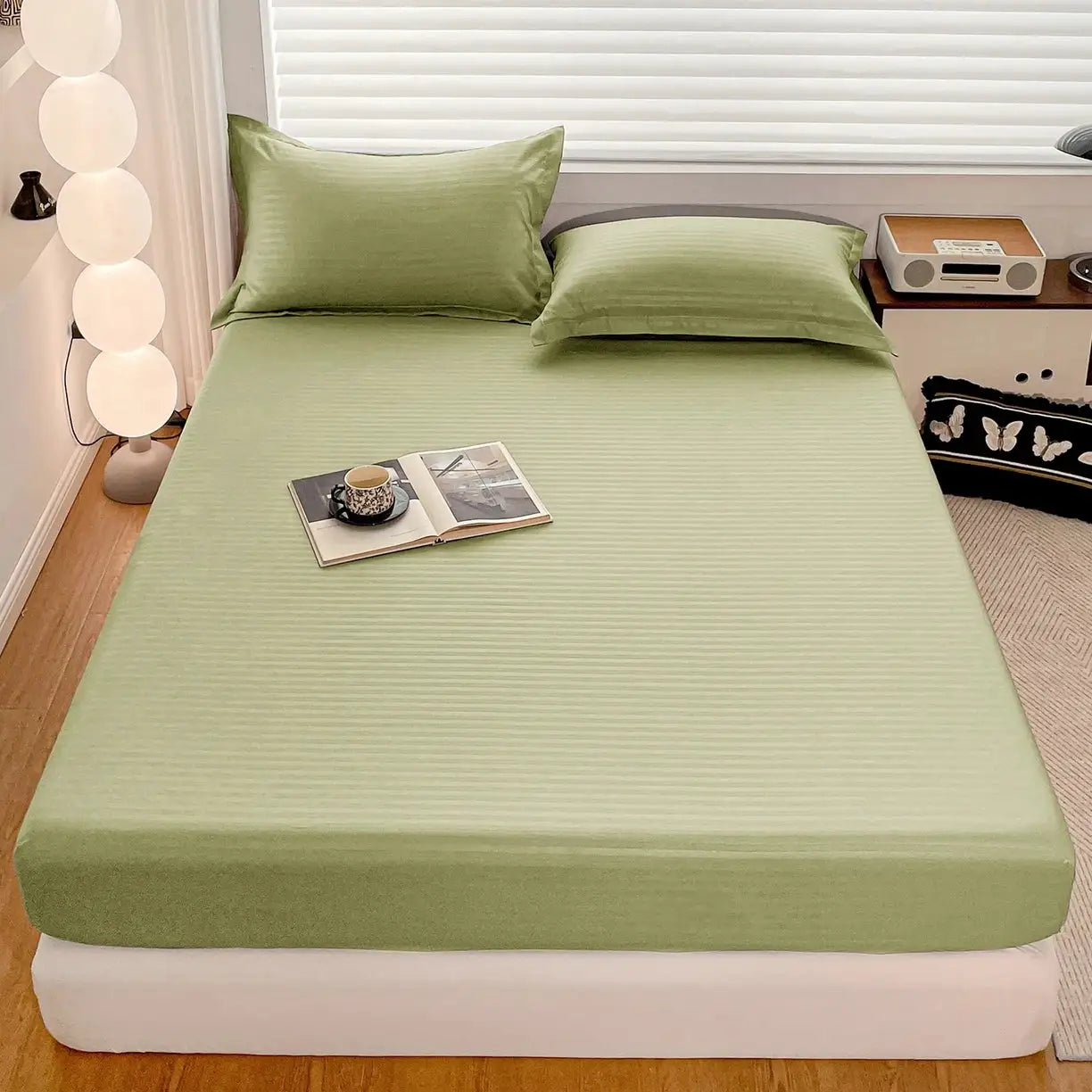 Fitted bed sheet with elastic band in sage green by Simples Market on a bed with two pillows