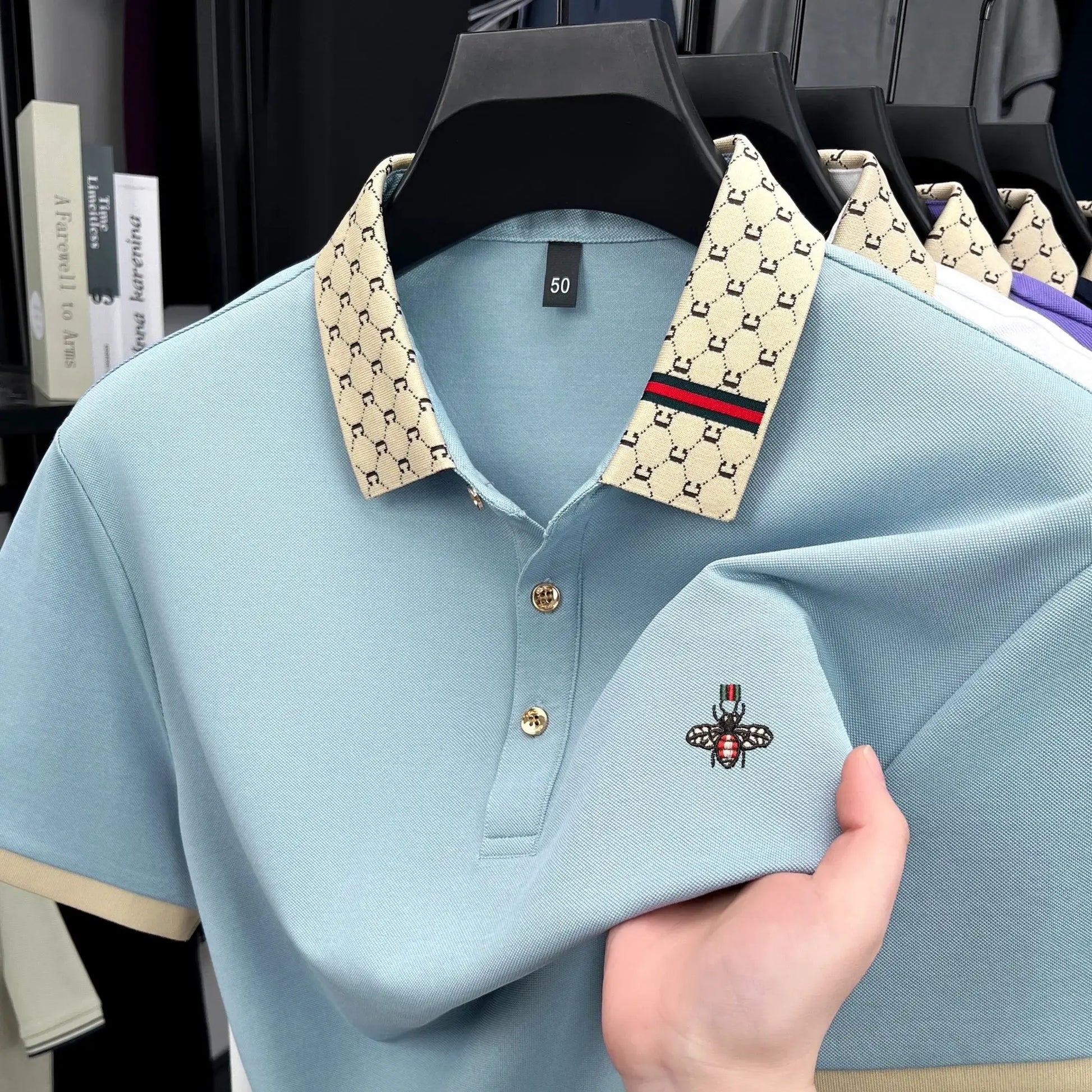 Men's light blue short-sleeve polo with beige letter jacquard collar and bee embroidery.
