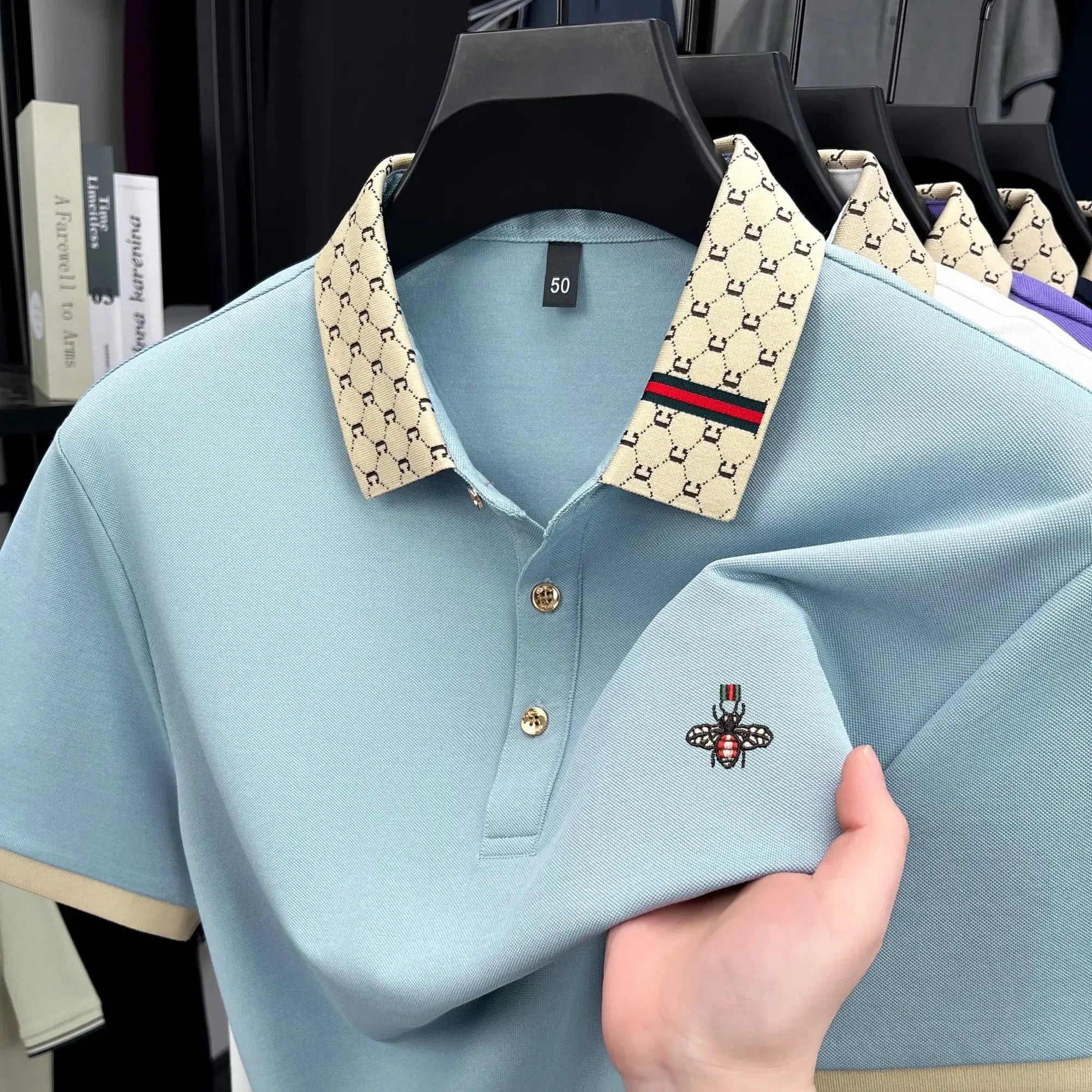 Men's light blue short-sleeve polo with beige letter jacquard collar and bee embroidery.