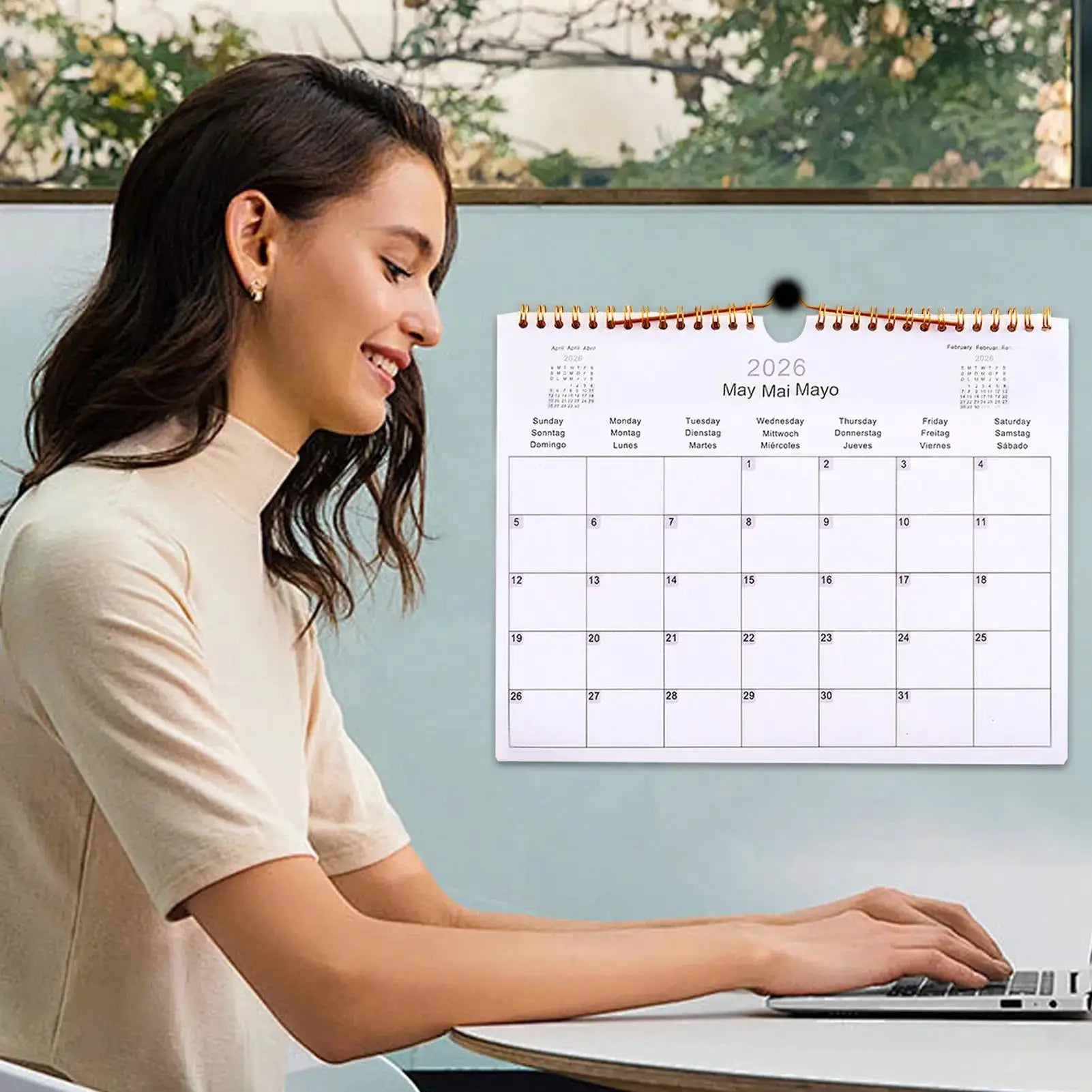 2026 multilingual wall calendar with copper coil binding by Simples Market, shown on a desk beside a laptop.