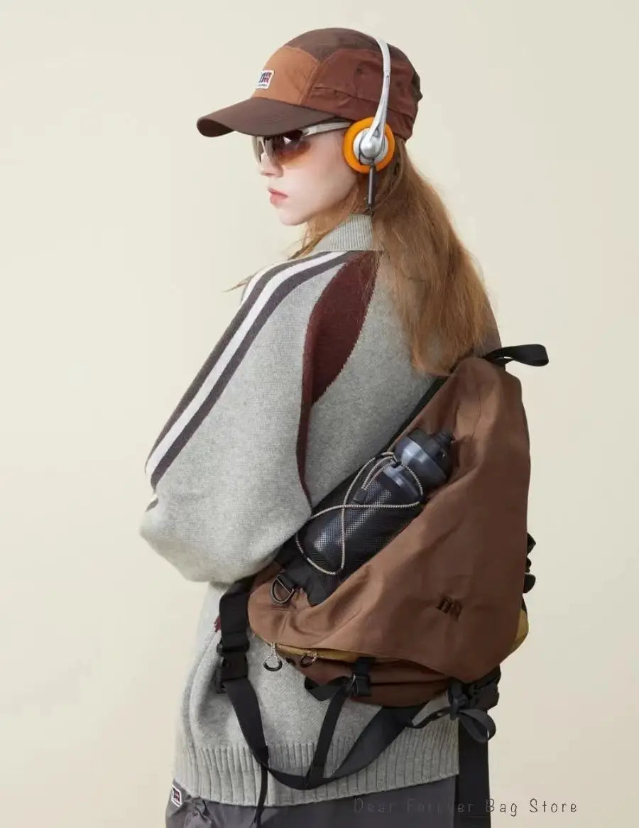 Brown nylon crossbody backpack with water bottle pocket, worn by a model in a gray striped sweater and brown cap