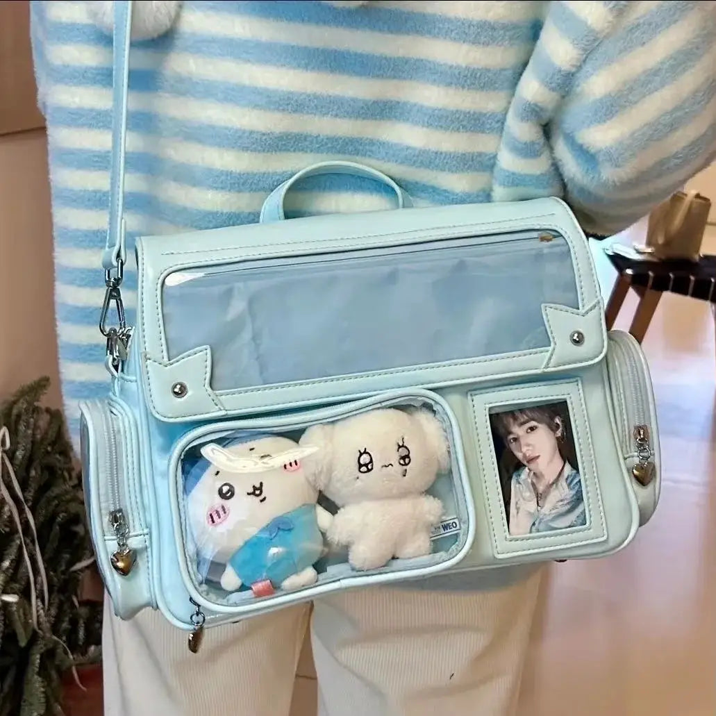 Ita bag crossbody in light blue with transparent pockets, two plush toys visible and a photo display