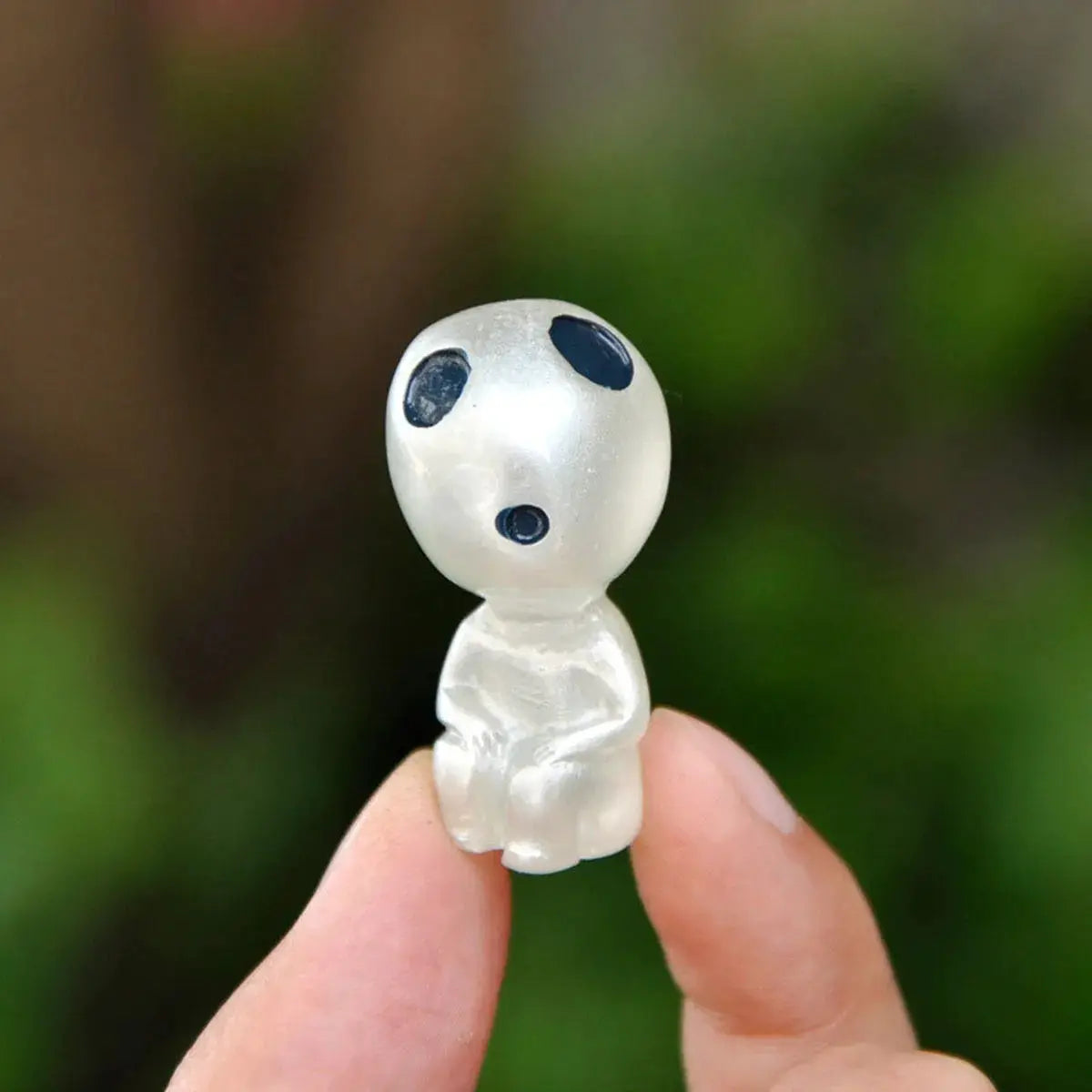 Miniature princess-shaped landscape ornament, translucent white figure with large black eyes, held between fingers.