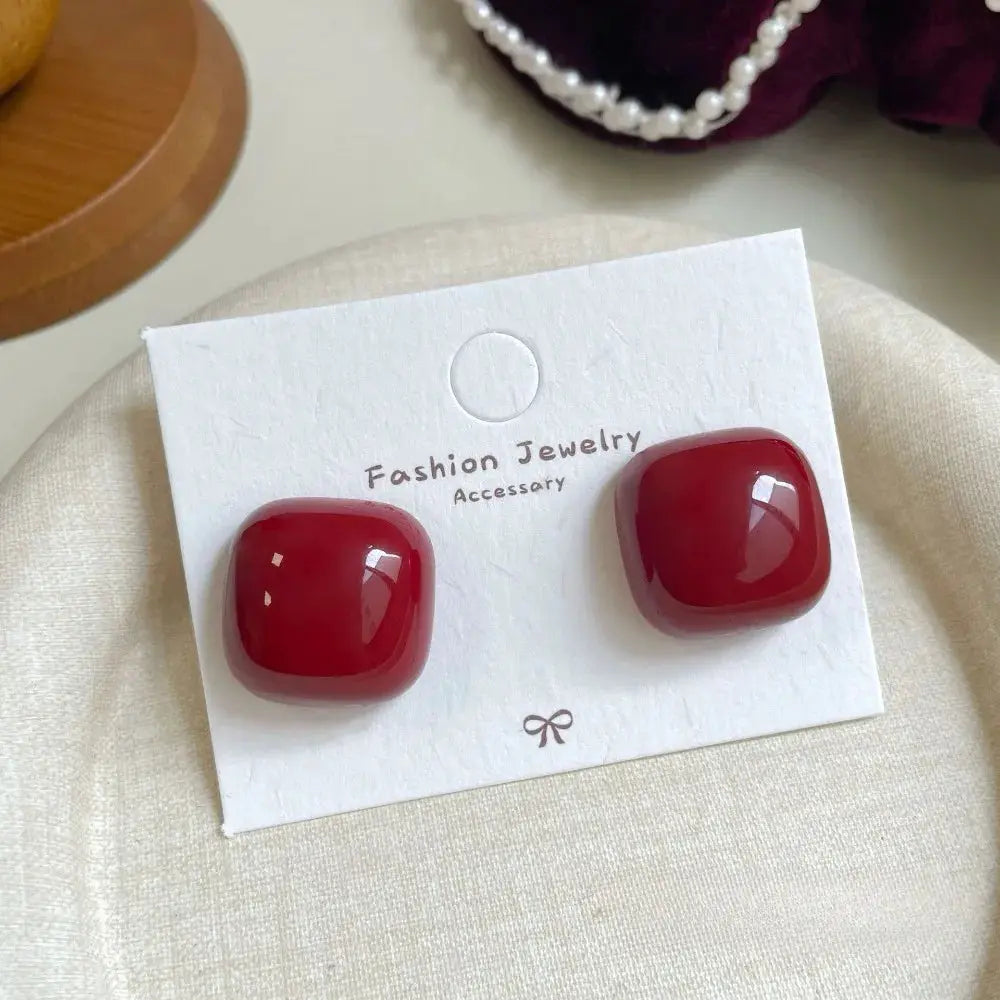 Two red glossy square stud earrings on a white card, fashion jewelry accessory.