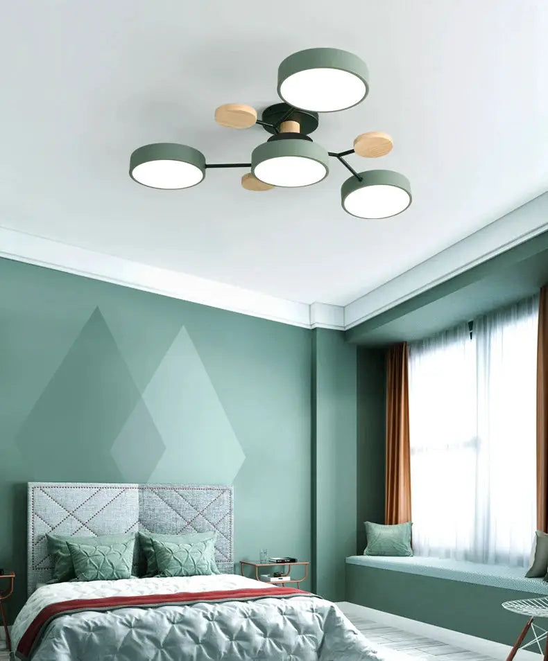 Modern LED ceiling chandelier with green circular shades and wooden accents in a green-toned bedroom.