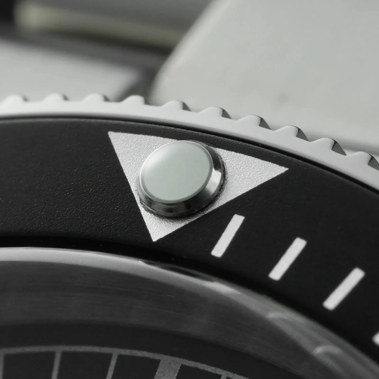 Watch crown close-up on a black diver bezel with white markers; silver stainless steel case