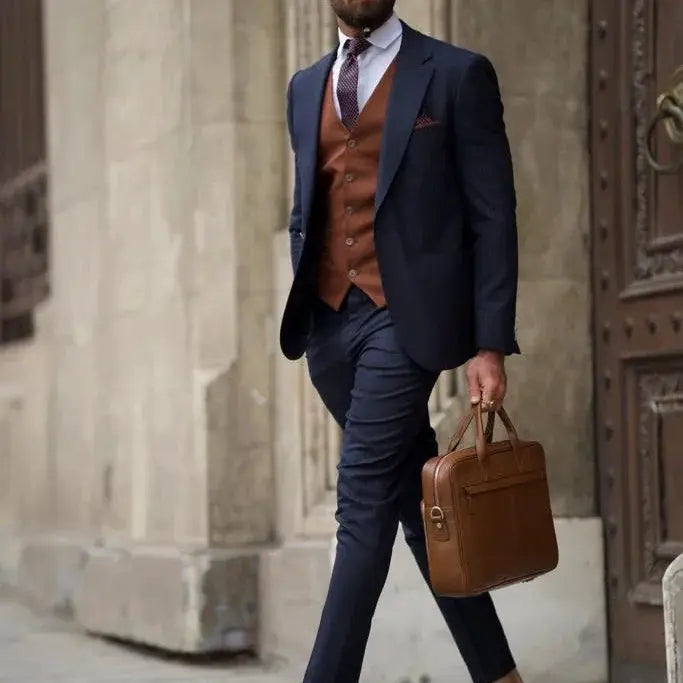 Men's navy slim-fit suit with brown waistcoat, light blue shirt, burgundy tie, and brown briefcase.