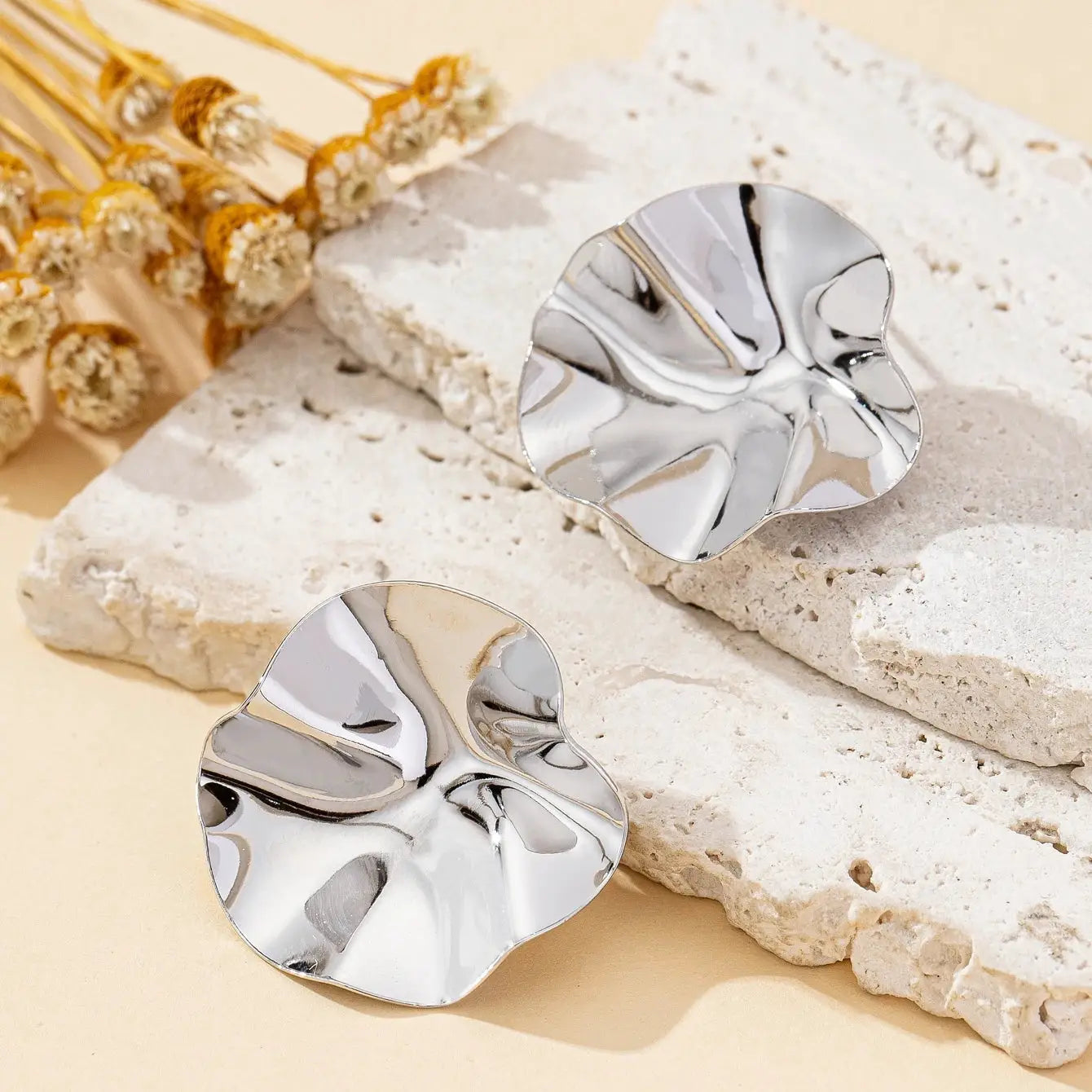 Pair of irregular round silver metal stud earrings on a beige stone backdrop