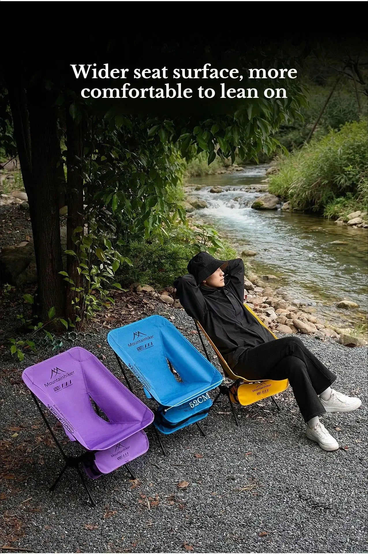 Foldable camping Moon chairs set in purple, blue, and yellow by a river; Mountainhiker branding visible, person relaxing in a black jacket.